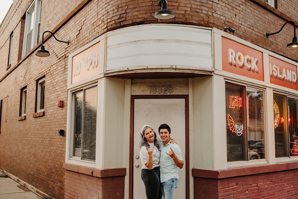 A couple stand outside the front door of a bar in Chicago and smile at the camera that's taking their engagement photos