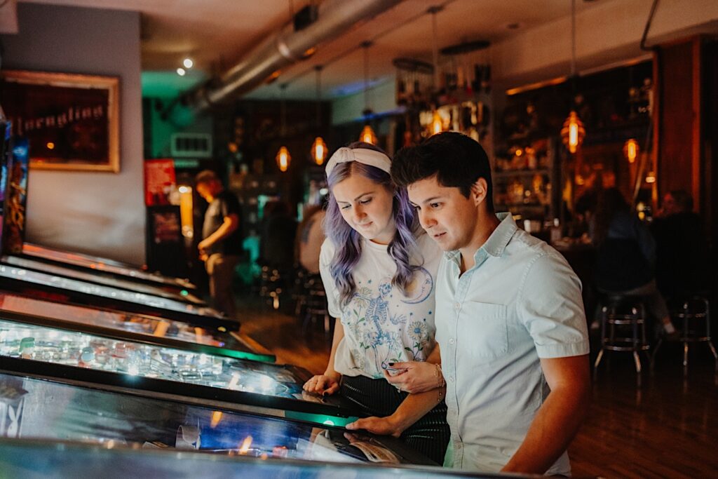 A couple in a bar in Chicago play pinball together while having their engagement photos taken