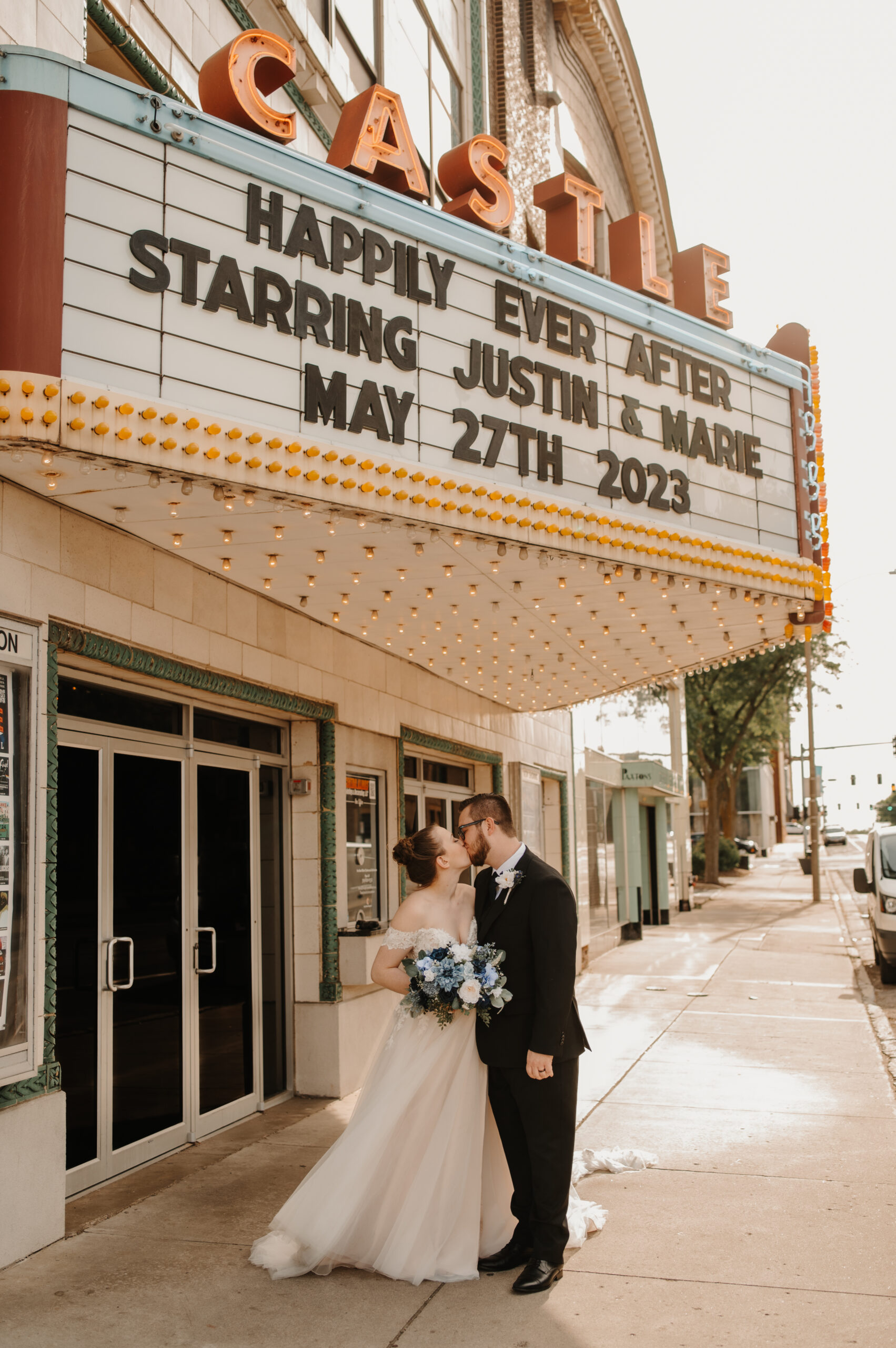 bride and groom pose for photos and kiss before their wedding underneath the castle theatre marquee in bloomington illinois
